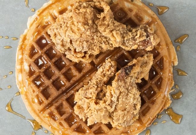 Large round waffle with two pieces of Fried Chicken on Top and Maple Syrup 