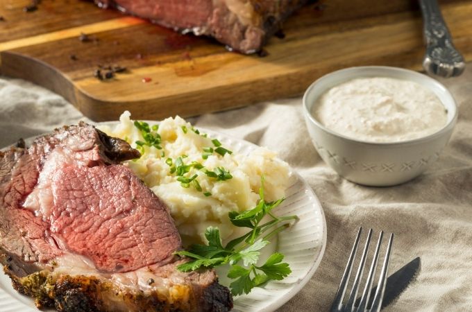 Slice of Prime rib on a plate with a side of mashed potatoes and a bowl of creamy horseradish sauce on the side 